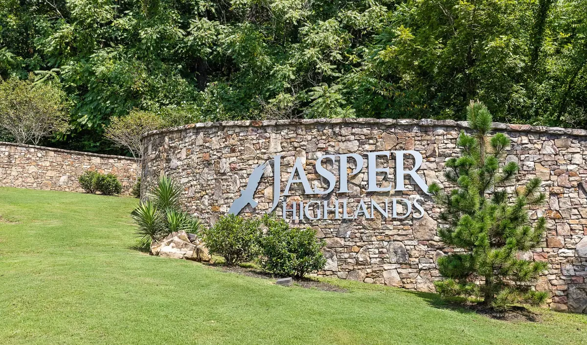 The main entrance of Jasper Highlands, with a welcoming stone wall, prominent signage, and lush, landscaped greenery. The setting is tranquil and open, evoking the feeling of entering a serene mountain retreat.
