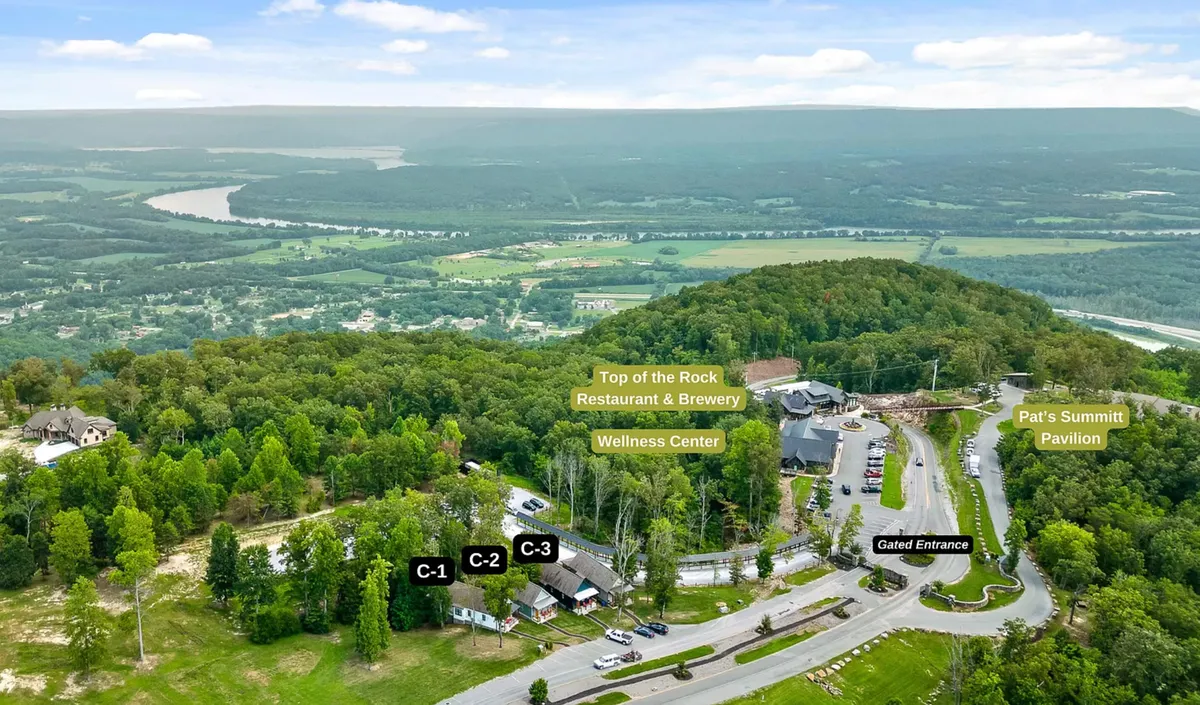 This exterior image features the Top of the Rock Restaurant & Brewery, the nearby Wellness Center, Pat's Summit Pavilion, and the gated entrance, all set against a backdrop of scenic landscape. The atmosphere is welcoming, highlighting the convenience of having dining and event venues just steps from the cottages.