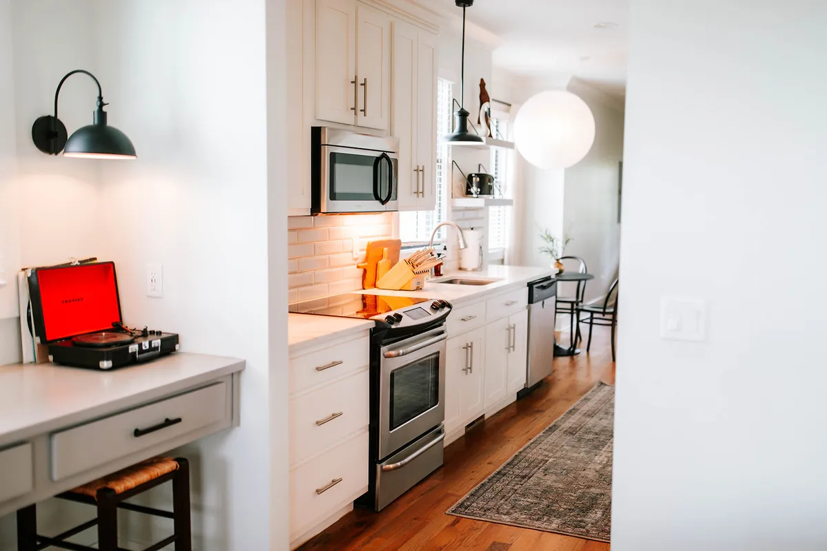A harmonious kitchen scene with visible appliances, a record player, warm lighting fixtures, and decorative shelving, evoking a cozy yet modern ambiance perfect for cooking, dining, or entertaining guests.