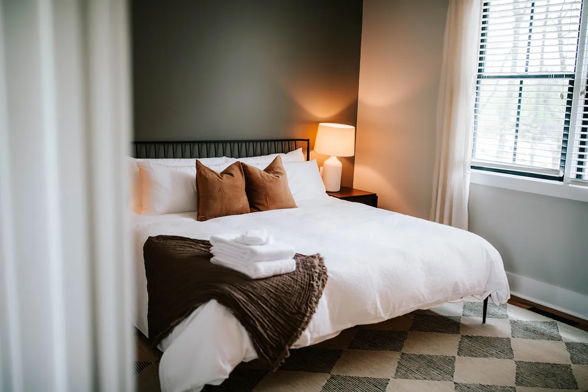 A serene bedroom featuring a comfortable bed, soft lighting from a bedside lamp, and a window that lets in gentle natural light. The tranquil setting is enhanced by plush bedding and restful décor, creating an inviting space to unwind.
