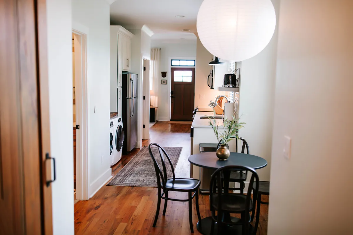 A cozy round dining table with chairs is set adjacent to kitchen appliances and an entrance door, inviting guests to settle in for casual or festive meals. The setup encourages intimate dinners or group celebrations, capturing the communal spirit of the dining area.
