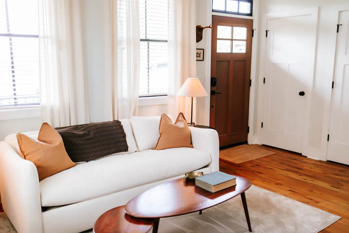 A bright, inviting entryway and living area, anchored by a white sofa and wooden coffee table. The front door is visible, suggesting a seamless flow from the entry into the main living space. Soft lighting and thoughtful décor create a welcoming first impression.